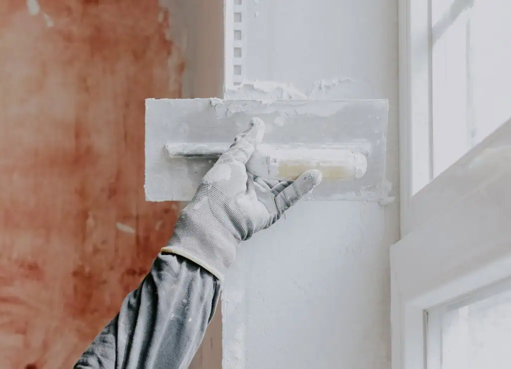 Wall plastering process with trowel and gloves for smooth finish.